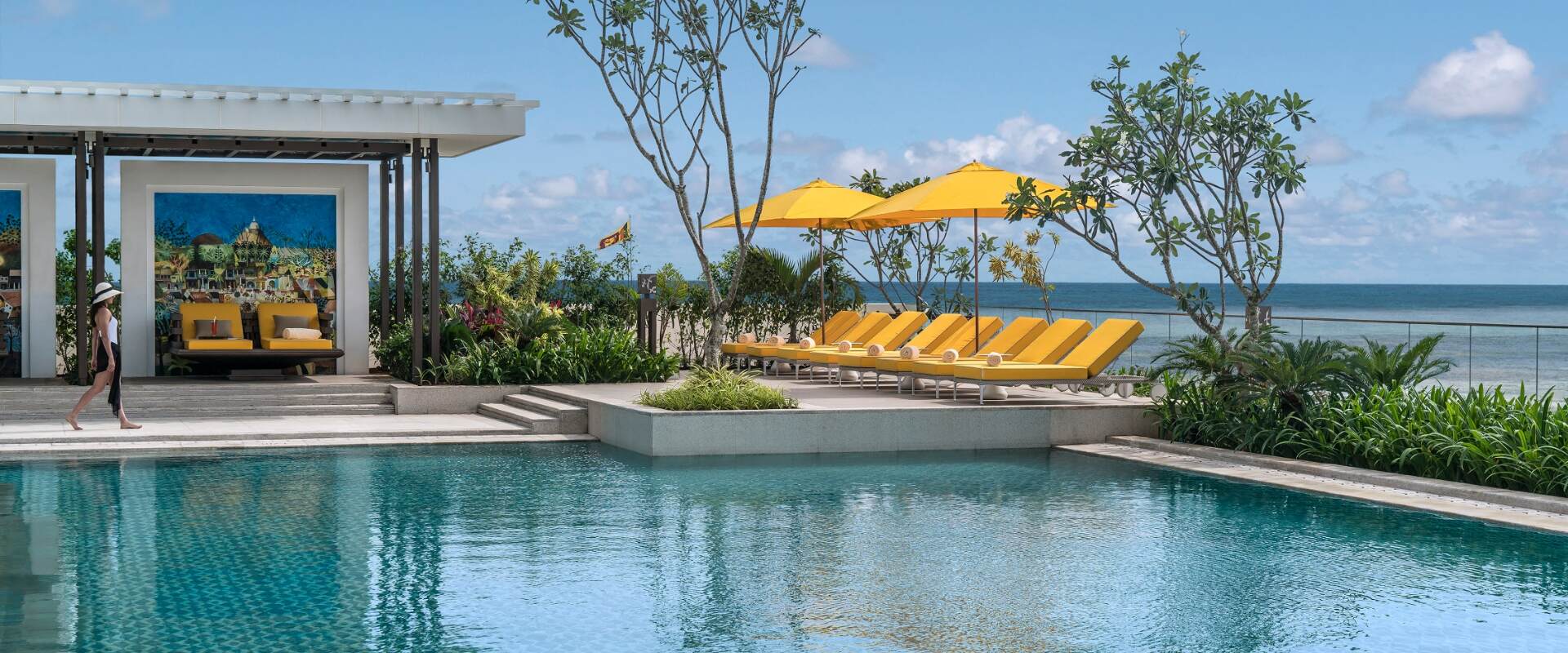 The pool terrace at water level, yellow sun loungers and frangipani trees against the ocean